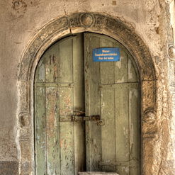 Sehr alte Holztür mit Stein und Schild.